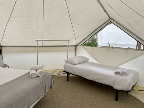 Vista interior de una tienda safari Bell Tent Plus con dos camas hechas, almohadas y toallas enrolladas.