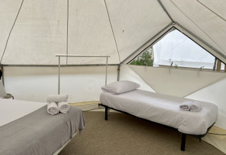 Interior view of a Bell Tent Plus safari tent with two made beds, pillows, and rolled-up towels on each.