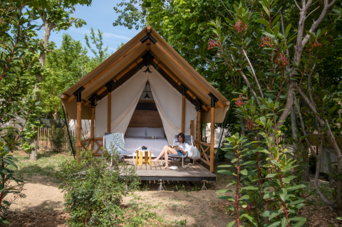 Iemand ontspant voor een safaritent bij Glamping Couple, omringd door groen en bomen.