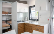 Modern glamping accommodation with kitchenette, dining area, and bedroom featuring bunk and double bed.