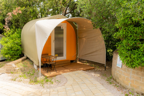 Safari-Zelt Coco Couple mit kleiner Terrasse, Tisch und Stühlen, umgeben von Bäumen und Natur.