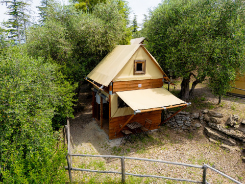 La tente safari Air Stay XL se trouve parmi les arbres, avec terrasse et petit jardin clôturé en bois.