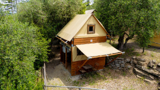 La tente safari Air Stay XL se trouve parmi les arbres, avec terrasse et petit jardin clôturé en bois.