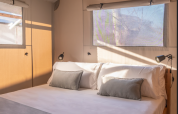 Cozy safari tent bedroom with a double bed, pillows, and sunlight streaming through window coverings.