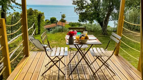 Wooden terrace of a safari tent with a breakfast table overlooking the lake at Vacanze Glamping Boutique, Italy.