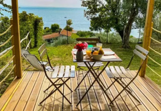Wooden terrace of a safari tent with a breakfast table overlooking the lake at Vacanze Glamping Boutique, Italy.