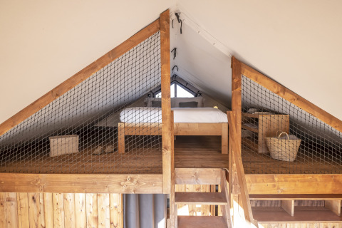 Houten loftslaapkamer met bed en manden in Lodge 'Family Duplex' bij Wecamp Santa Cristina, Spanje.