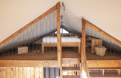 Wooden loft bedroom with bed, baskets, and shelving in Lodge 'Family Duplex' at Wecamp Santa Cristina, Spain.