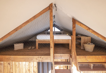 Dormitorio tipo altillo de madera con cama y cestas en Lodge 'Family Duplex' de Wecamp Santa Cristina, España.
