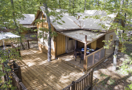 Luxuriöses Safari-Zelt Air Dreamer 2 im Wald mit großer Holzterrasse und gemütlichem Essbereich.
