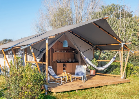 Safari tent Lodge Grand Family met houten veranda, hangmat, stoelen en buitenkeuken in groene natuur.