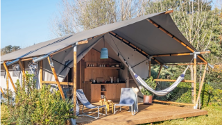Safari tent Lodge Grand Family with wooden veranda, hammock, chairs, and outdoor kitchen in green nature.