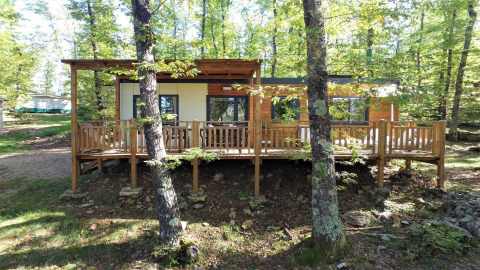 Casa piccola chiamata Cottage Next L con terrazza in legno, immersa in una foresta verde tra gli alberi.