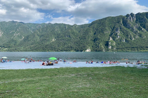 Des personnes profitent de la plage du Lago Idro Glamping Boutique entourée de montagnes vertes en Lombardie.