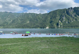 Des personnes profitent de la plage du Lago Idro Glamping Boutique entourée de montagnes vertes en Lombardie.