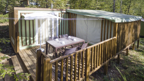 Buitenterras bij Cottage Clever lodge met tafel, stoelen en parasol, omringd door groene bomen.