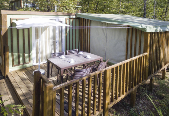 Buitenterras bij Cottage Clever lodge met tafel, stoelen en parasol, omringd door groene bomen.