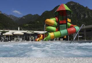 Udsigt over en swimmingpool med farverige vandrutsjebaner og bjerge i baggrunden på Lago Idro Glamping Boutique.