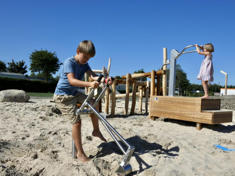 Twee kinderen spelen op een zand-speelplein met speeltuigen aan een glampingplek bij mooi weer.