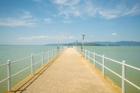 Vista dal pontile del Trasimeno Glamping Resort in Umbria, Italia, con il lago e le colline sullo sfondo.