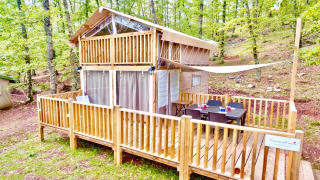 Airlodge 1 in het bos, een houten tweelaags lodge met terras, buitentafel en omgeven door groene bomen.