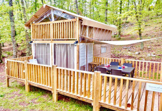 Airlodge 1 nestled in the forest, two-story wooden cabin with deck, outdoor dining table, and lush trees.