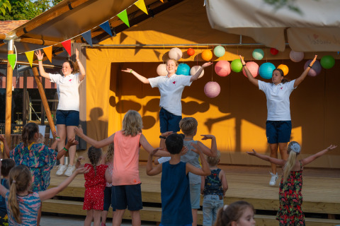 Children dancing with instructors on a stage at Trasimeno Glamping Resort in Umbria, Italy, in the sunlight.