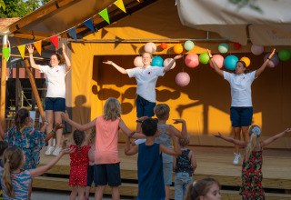 Bambini che ballano con animatori sul palco al Trasimeno Glamping Resort in Umbria, Italia, alla luce del sole.
