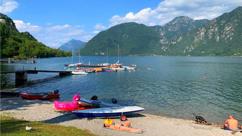 Vista del lago Idro con barcos, montañas verdes y personas relajándose en la orilla en Lombardía, Italia.