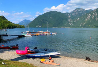 Vista del lago Idro con barcos, montañas verdes y personas relajándose en la orilla en Lombardía, Italia.