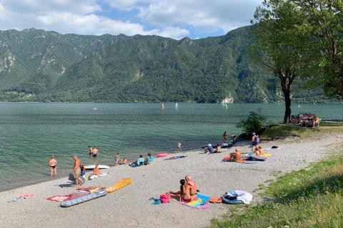 Folk nyder solen og svømmer ved søen Lago Idro i Lombardiet, Italien, med bjerge i baggrunden.