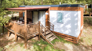 Buitenaanzicht van de Cottage Next-lodge met houten veranda, zitgedeelte en omringd door bomen.
