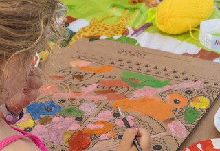 Una bambina dipinge su cartone a un tavolo con animali al Lago Idro Glamping Boutique in Lombardia, Italia.