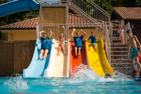 Kids and adults enjoying colorful waterslides into the pool at Trasimeno Glamping Resort in Umbria, Italy.