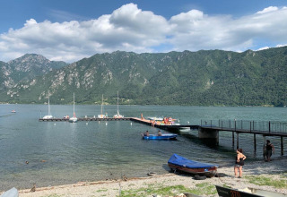 Steiger en boten aan Lago Idro Glamping Boutique in Lombardije, Italië, met bergen en bezoekers op de achtergrond.