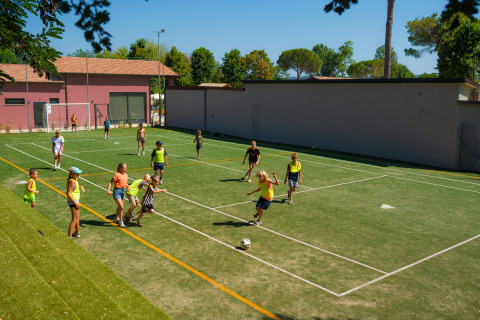 Children playing soccer on a sunny sports field at Trasimeno Glamping Resort holiday park in Umbria, Italy.