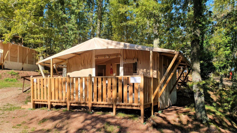 Tenda lodge deluxe con veranda in legno, immersa tra gli alberi in un campeggio boscoso e soleggiato.