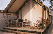 Safari-Zelt mit Bambusrahmen und Holzterrasse, ausgestattet mit Gartenmöbeln, auf Kies gelegen.