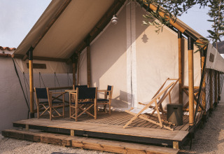 Safari tent met bamboeframe en houten terras, voorzien van buitenstoelen en grind eromheen.