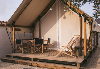 Tenda safari con struttura in bambù, veranda in legno e sedie da esterno, su ghiaia.