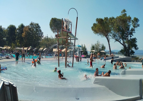Bambini e adulti giocano nella piscina e area giochi d’acqua a Trasimeno Glamping Resort in Umbria, Italia.