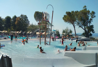 Bambini e adulti giocano nella piscina e area giochi d’acqua a Trasimeno Glamping Resort in Umbria, Italia.