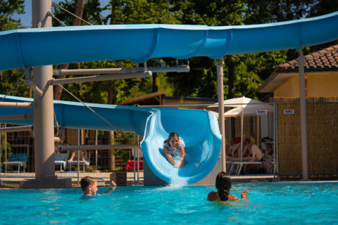 Children playing in the pool as a girl comes down a blue waterslide at Trasimeno Glamping Resort in Umbria, Italy.
