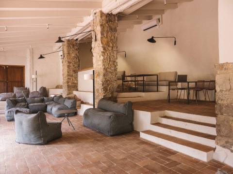 Zona lounge moderna al Wecamp Cala Montgó con poltrone sacco, colonne in pietra e atmosfera accogliente.