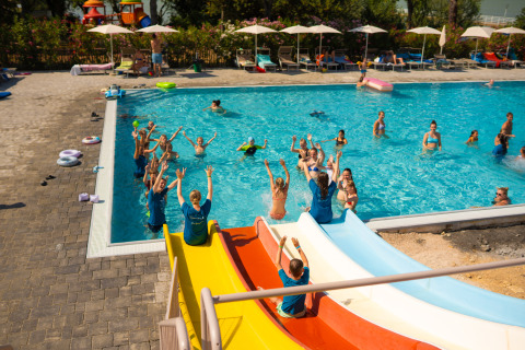 Children play in the pool and enjoy water slides at Trasimeno Glamping Resort in Umbria, Italy, on a sunny day.