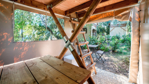 Vue de l'intérieur d'une tente safari avec table en bois, échelle et coin salon extérieur.