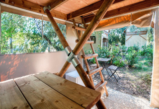 Vue de l'intérieur d'une tente safari avec table en bois, échelle et coin salon extérieur.