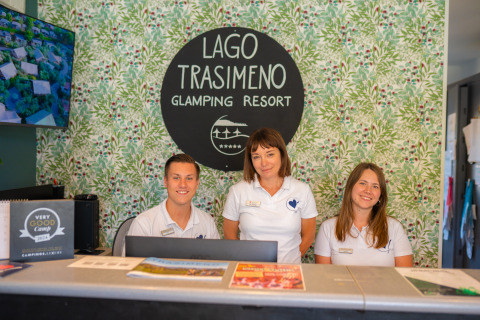 Reception staff at Trasimeno Glamping Resort in Umbria, Italy, smiling behind the desk ready to welcome guests.