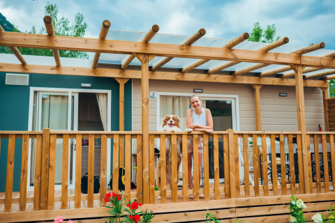 Femme et chien profitent sur la terrasse en bois devant le chalet Next XL Superior Dog avec des fleurs.