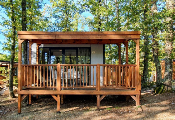 Vooraanzicht van Cube Suite-lodge met houten terras, midden in het bos en omgeven door groene bomen.